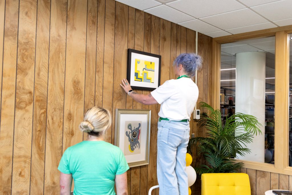 Sarah Heitkamp hangs artwork on a wood-paneled wall.