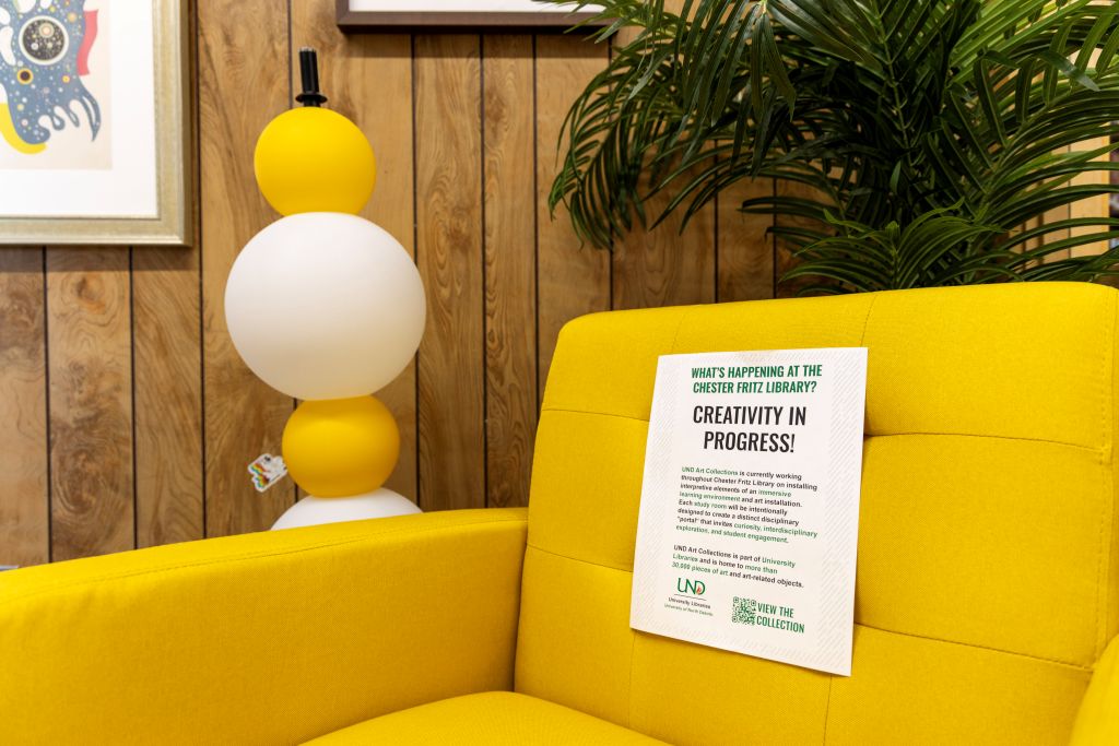 A sign with the words "Creativity in Progress" rests on a yellow chair.