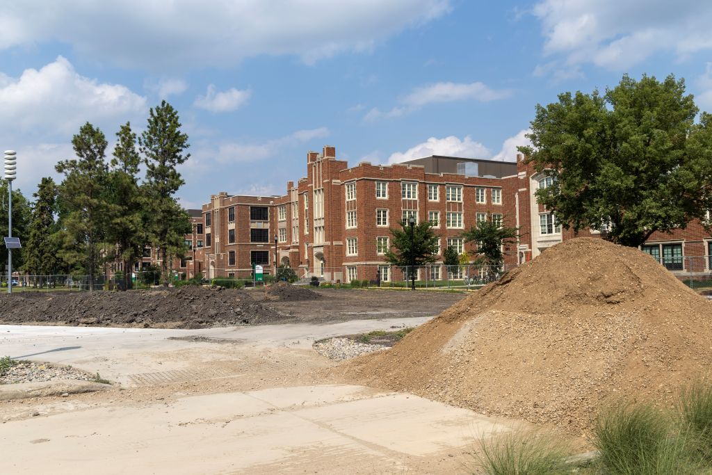 Pile of dirt next to darker soil of demolition site, buildings in background