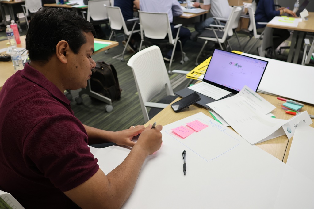 Man sitting at a table works on a poster, with a laptop open nearby.