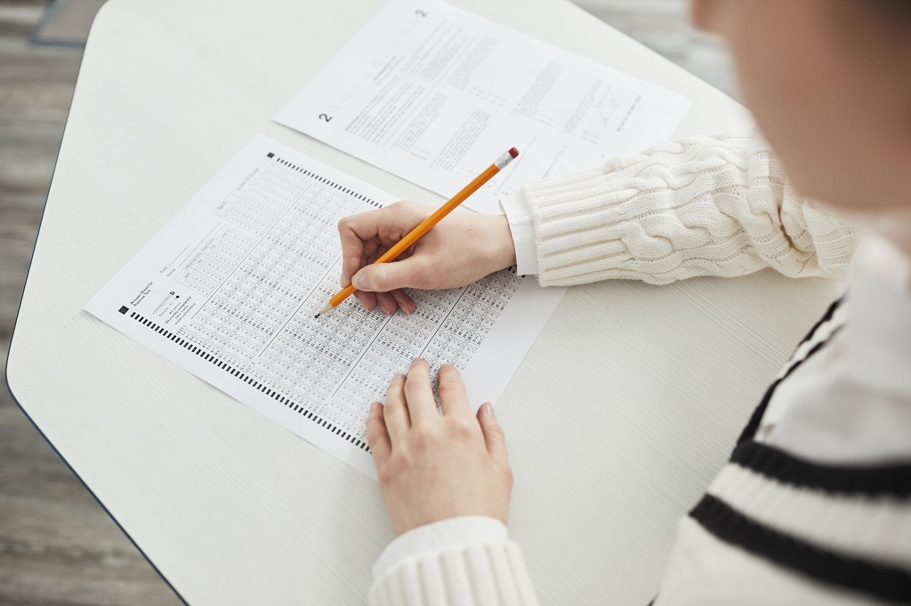 Student taking a test; only hand holding a pencil, and the test answer sheet are visibile