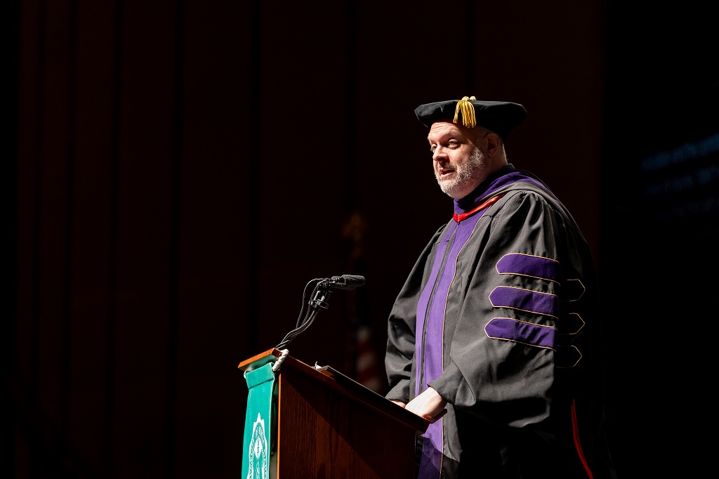 Man in academic regalia delivers a commencement speech
