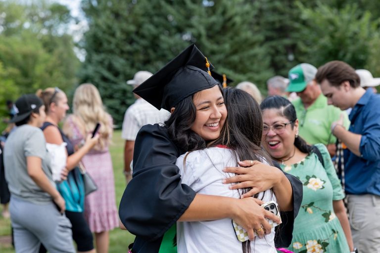 Woman wearing cap and gown hugs guest at Summer Commencement 2026
