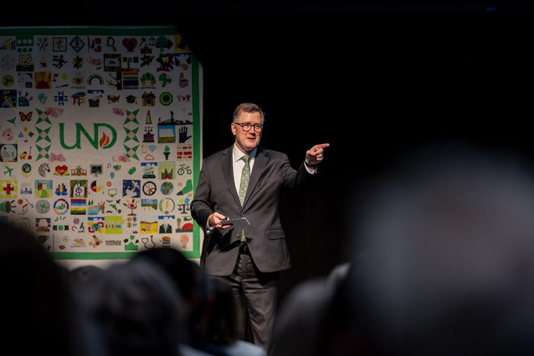 Andy Armacost points while speaking on stage at State of the University