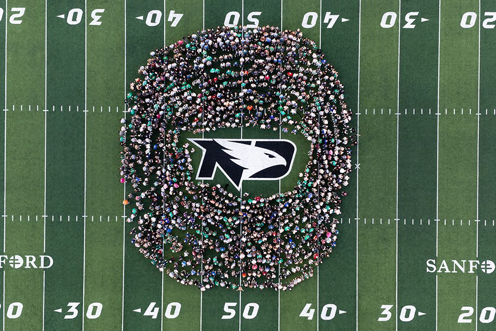 Aerial view of UND students gathered in a large circle around the Fighting Hawks logo at midfield inside the Alerus Center