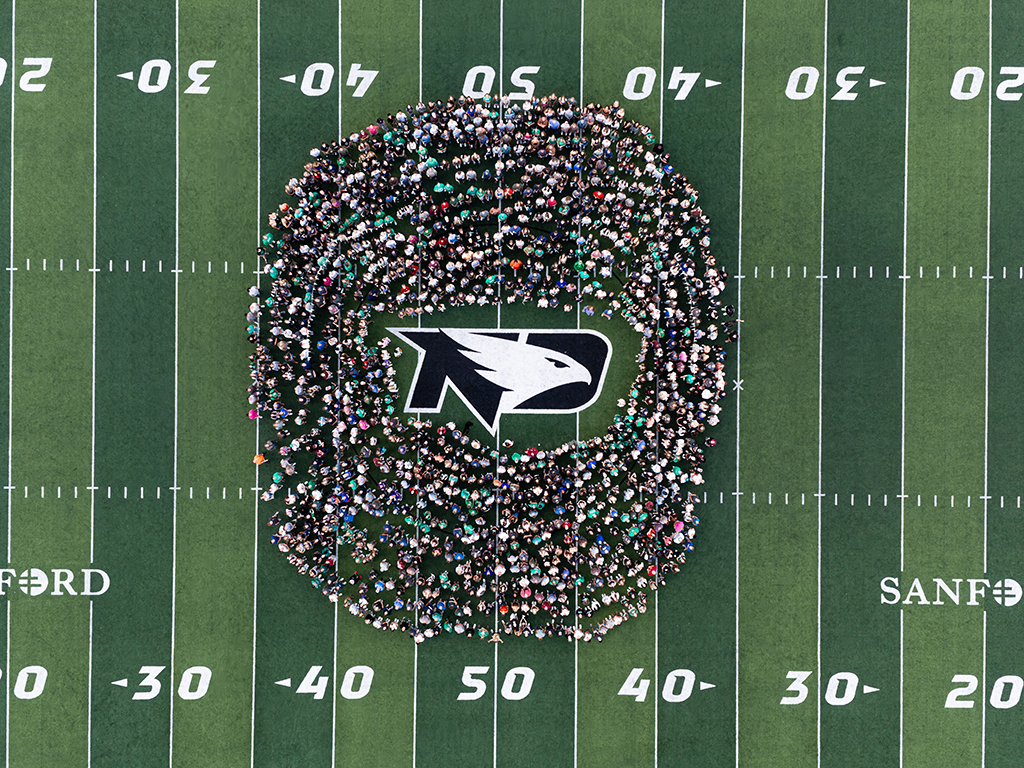Aerial view of UND students gathered in a large circle around the Fighting Hawks logo at Memorial Field