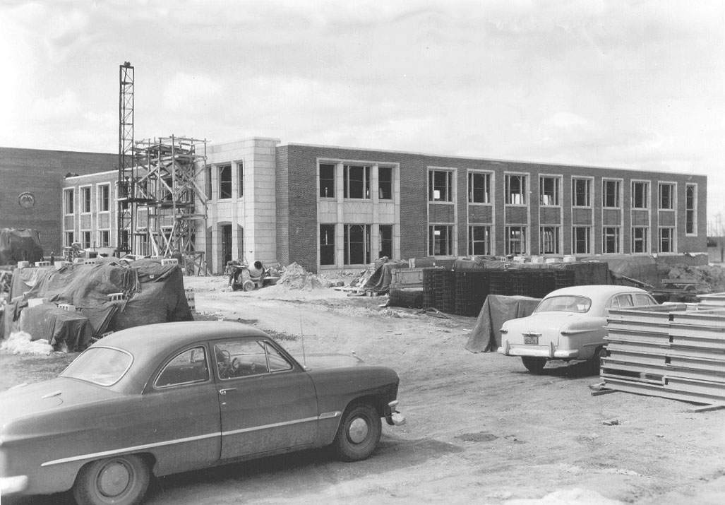 Historic black-and-white photograph of the Charles R. Robertson Lignite Research Laboratory under construction in 1949, showing the partially completed two-story brick building with scaffolding, construction materials and parked automobiles.
