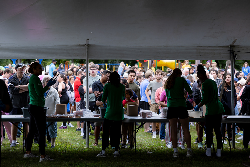 Volunteers serve food from beneath a large tent as a crowd waits in line at the Potato Bowl French Fry Feed.