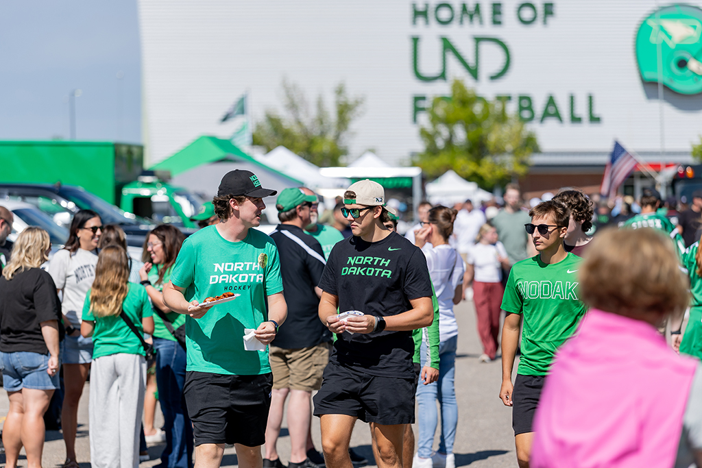Fans wearing UND green and black walk among tailgating tents, vehicles and crowds outside the Alerus Center.