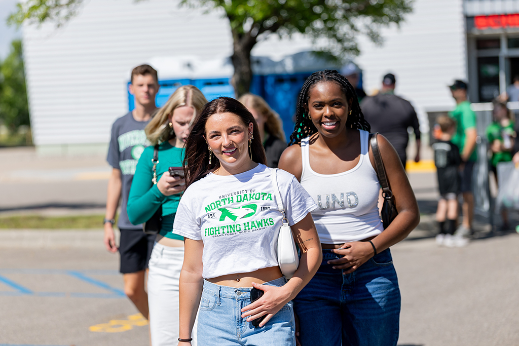 Two smiling fans wearing UND shirts walk through a crowd outside the Alerus Center.