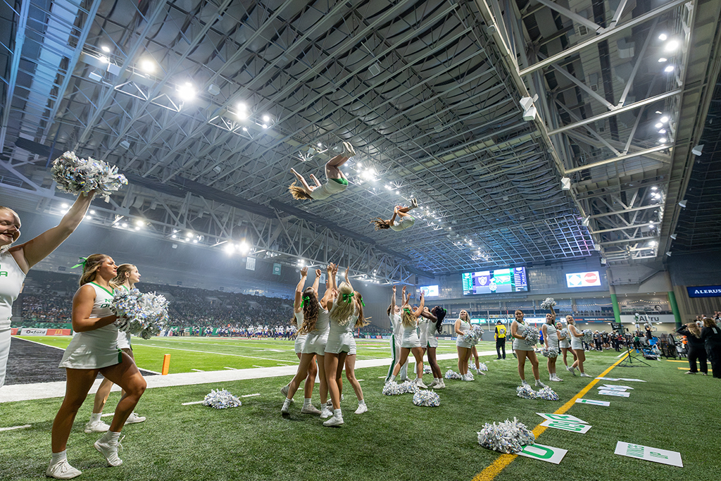 UND cheerleaders perform stunts along the sideline as two team members are tossed into the air.