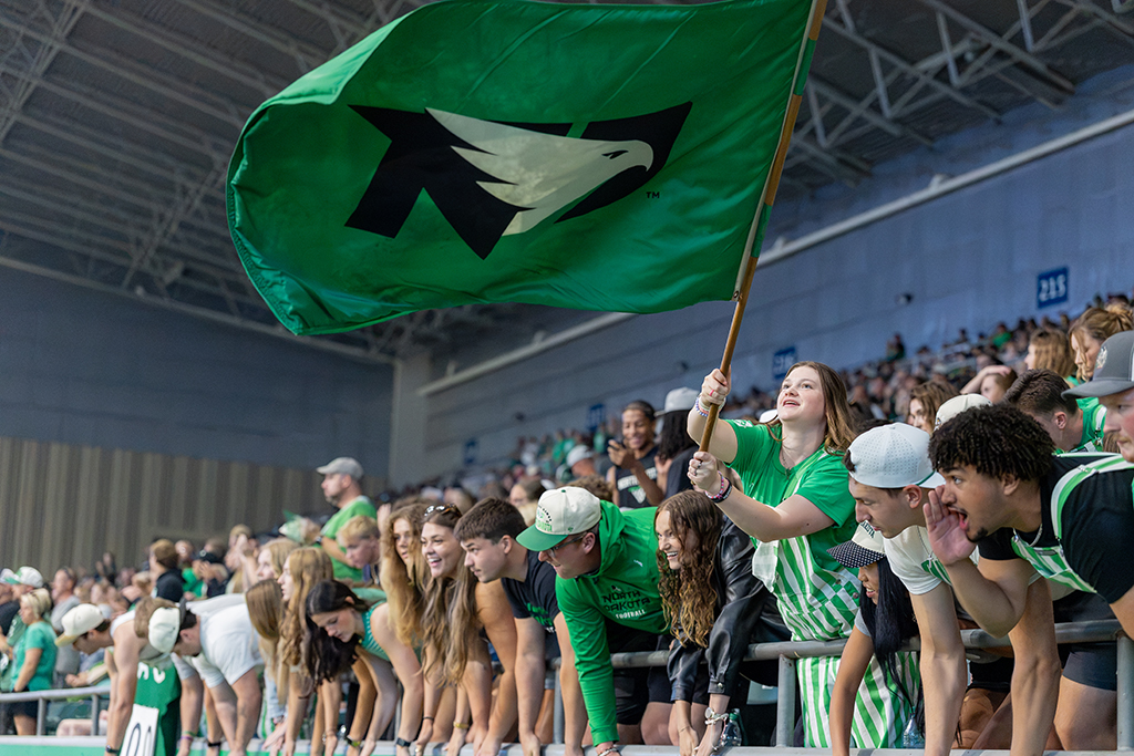 A student waves a large green UND Fighting Hawks flag above a cheering student section at the Alerus Center.