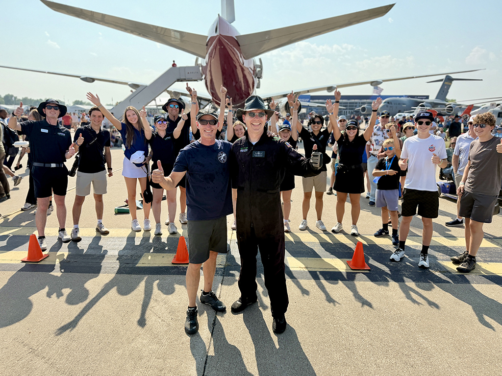 Jeff Boerboon and Michael Lents give thumbs-up as a group of aviation enthusiasts celebrates behind them at EAA AirVenture Oshkosh.