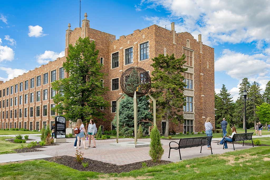 Students walk and gather outside on the UND campus near the eternal flame sculpture on a sunny day.