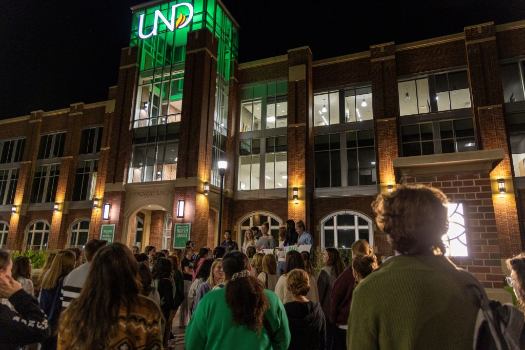 A crowd gathers outside the brightly lit Memorial Union at night.
