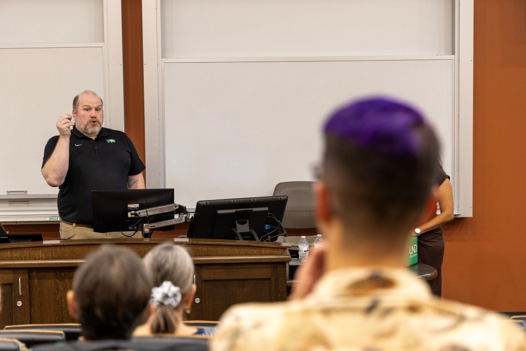 Jesse Rhoades speaks from the front of a classroom as audience members watch from their seats.