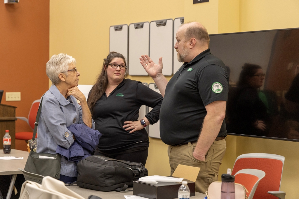 Jesse Rhoades gestures while speaking with two attendees in a classroom after his lecture.