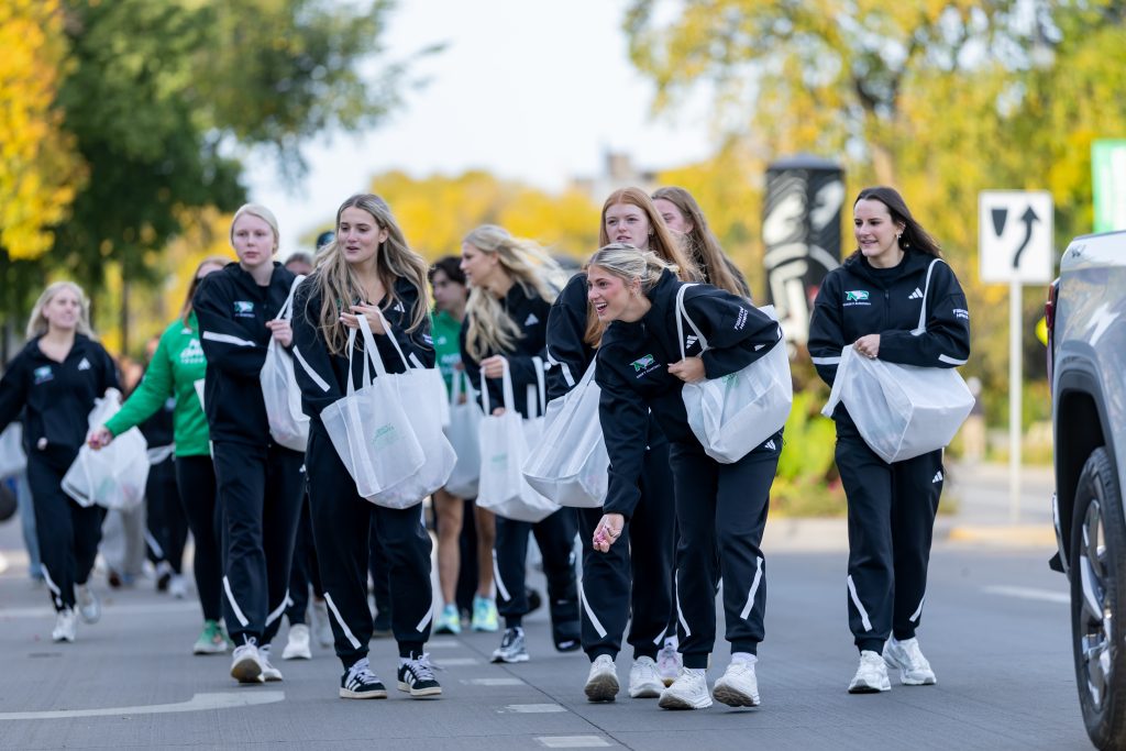 UND athletes walk along University Avenue during the Homecoming Parade, carrying bags and handing out candy to spectators.